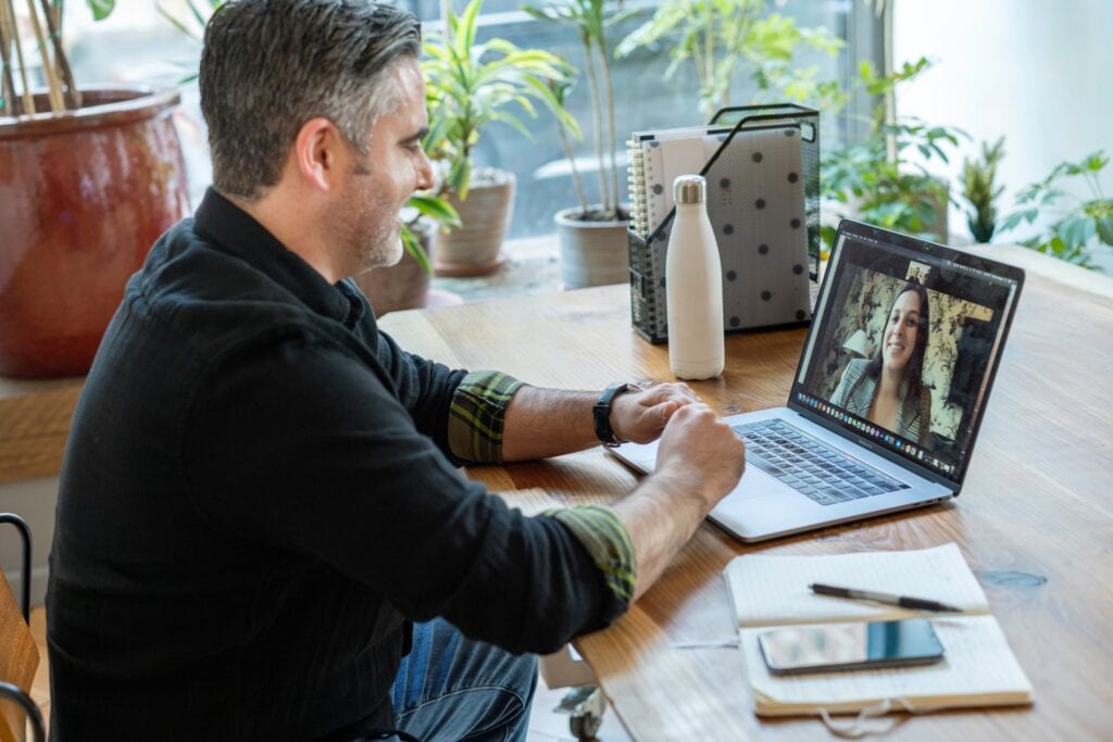 A man looking at a woman on the screen on a laptop having a therapy session