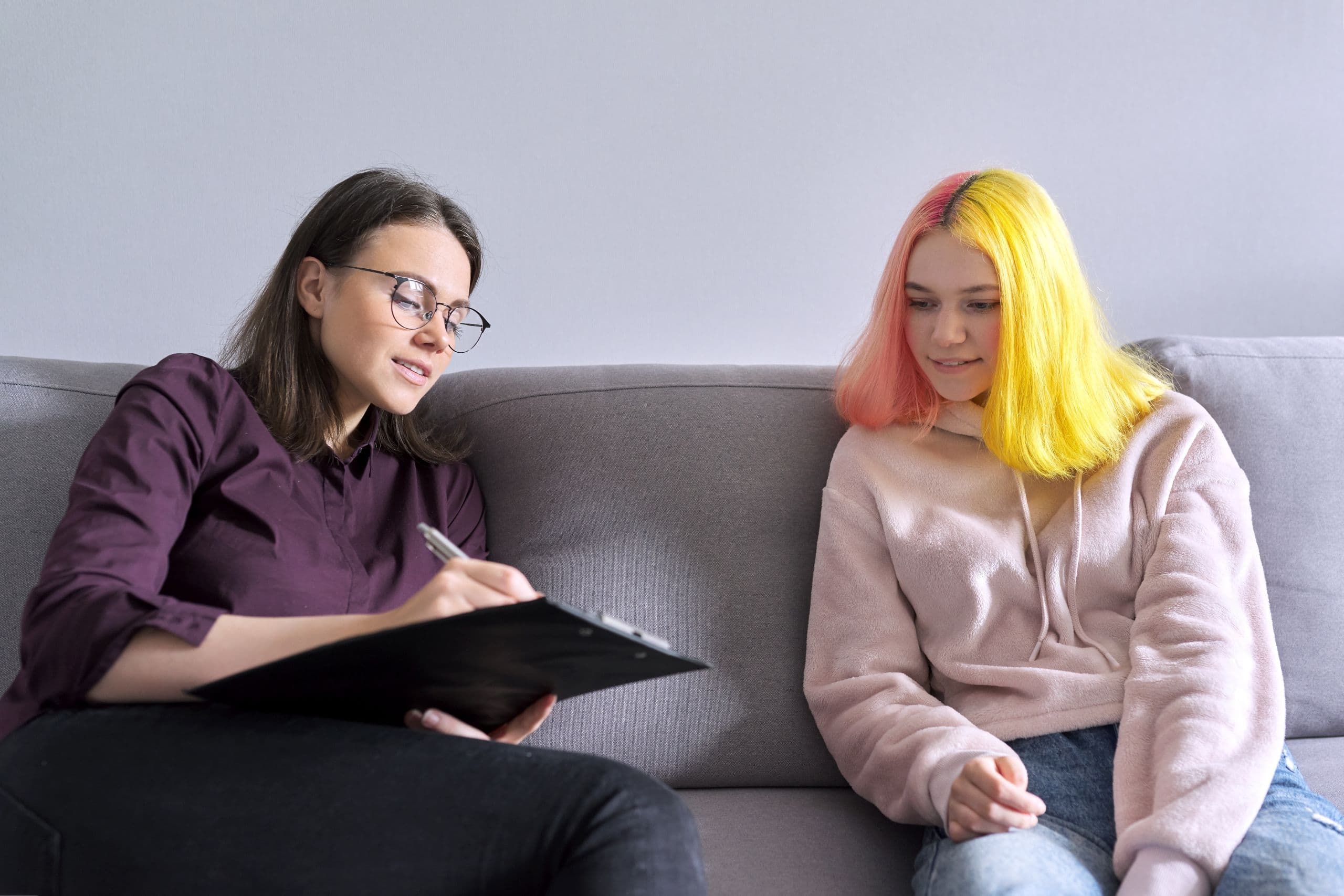 A counsellor and a young woman with bright hair sitting on a couch.